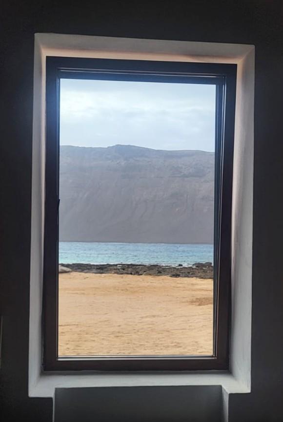 Vista desde una ventana enmarcando una playa volcánica y el mar con acantilados al fondo